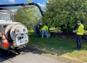 Two Washington Water employees excavating a service line for inspection in a wooded area